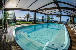 Piscina coberta com vista para o mar e palmeiras.