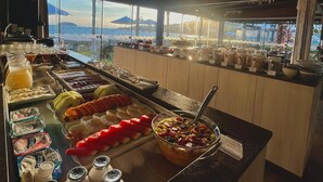 A buffet with various food items and beverages, a large decorative wheel, and a view of the sea through large windows. - Hotel Sete Ilhas (Florianópolis)