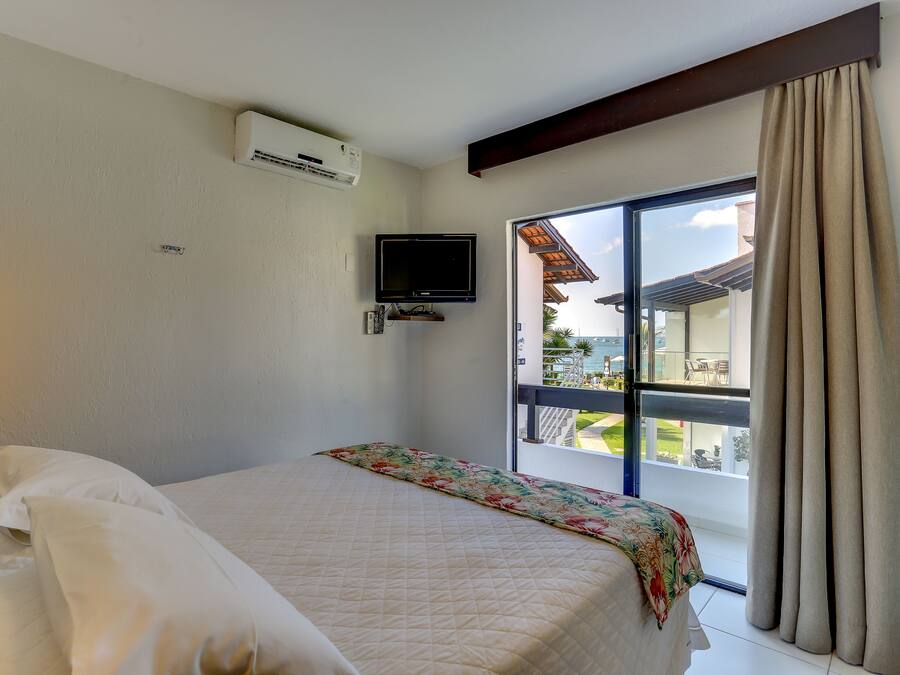 Habitación de hotel con cama, televisión montada en la pared y un amplio ventanal con cortinas.