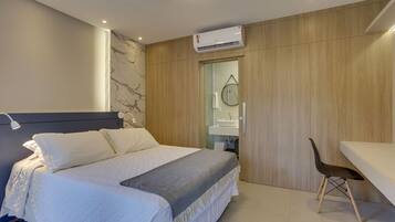 A modern bedroom with a bed, a desk, and a bathroom visible through an open door.