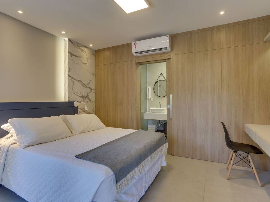 A modern bedroom with a bed, a desk, and a bathroom visible through an open door.