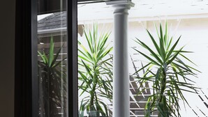 Habitació amb llit, finestra i vista a un balcó amb plantes en testos i una columna blanca.