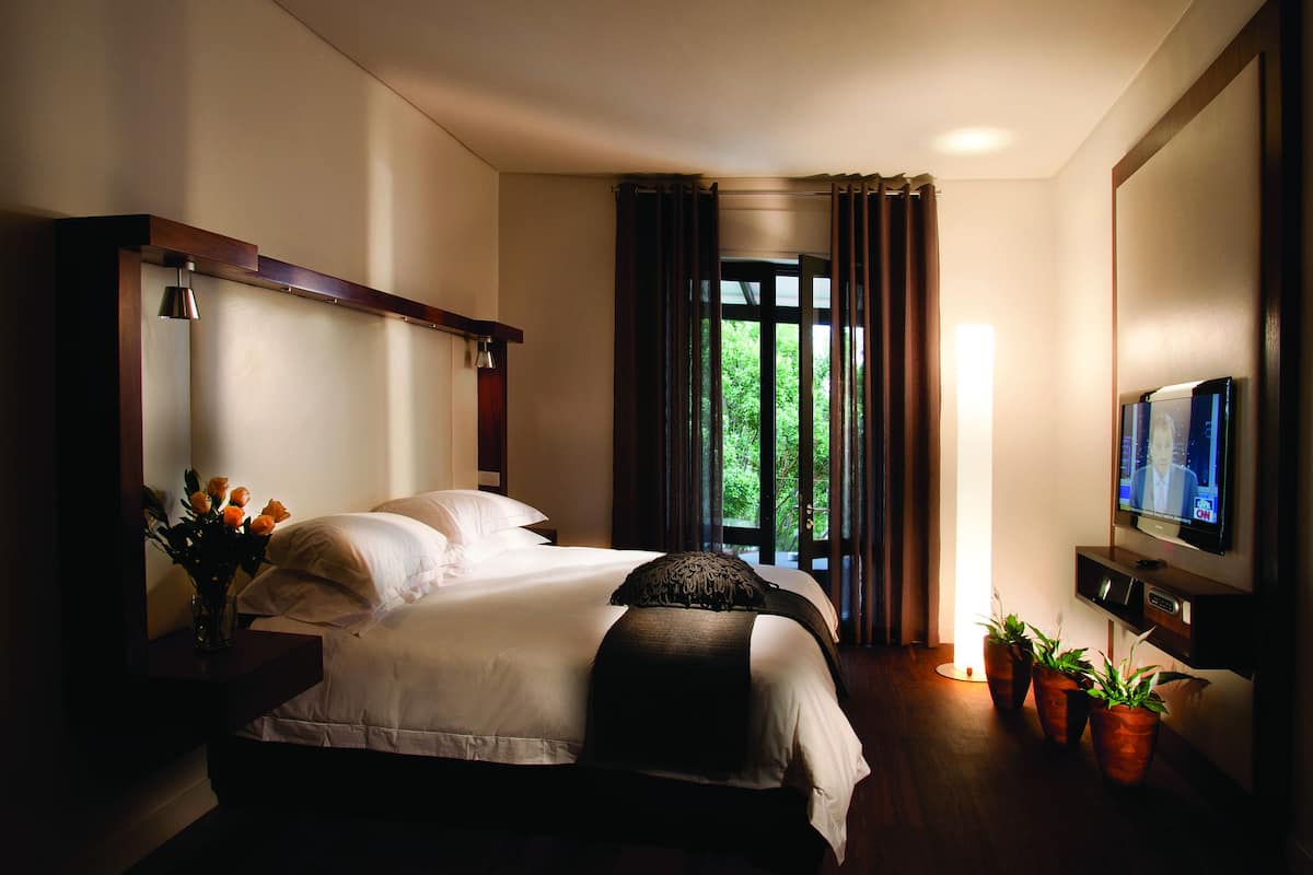 Habitación de hotel bien iluminada con una cama grande, televisión y ventana con cortinas.