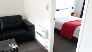 A hotel room with a black leather chair, a bed with a red blanket, and a white radiator.