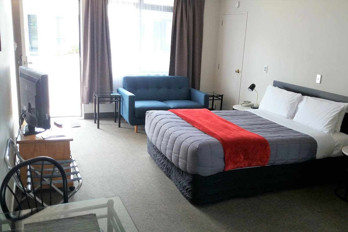 A hotel room with a bed, a blue armchair, a desk with a computer, and a view of the outdoors.