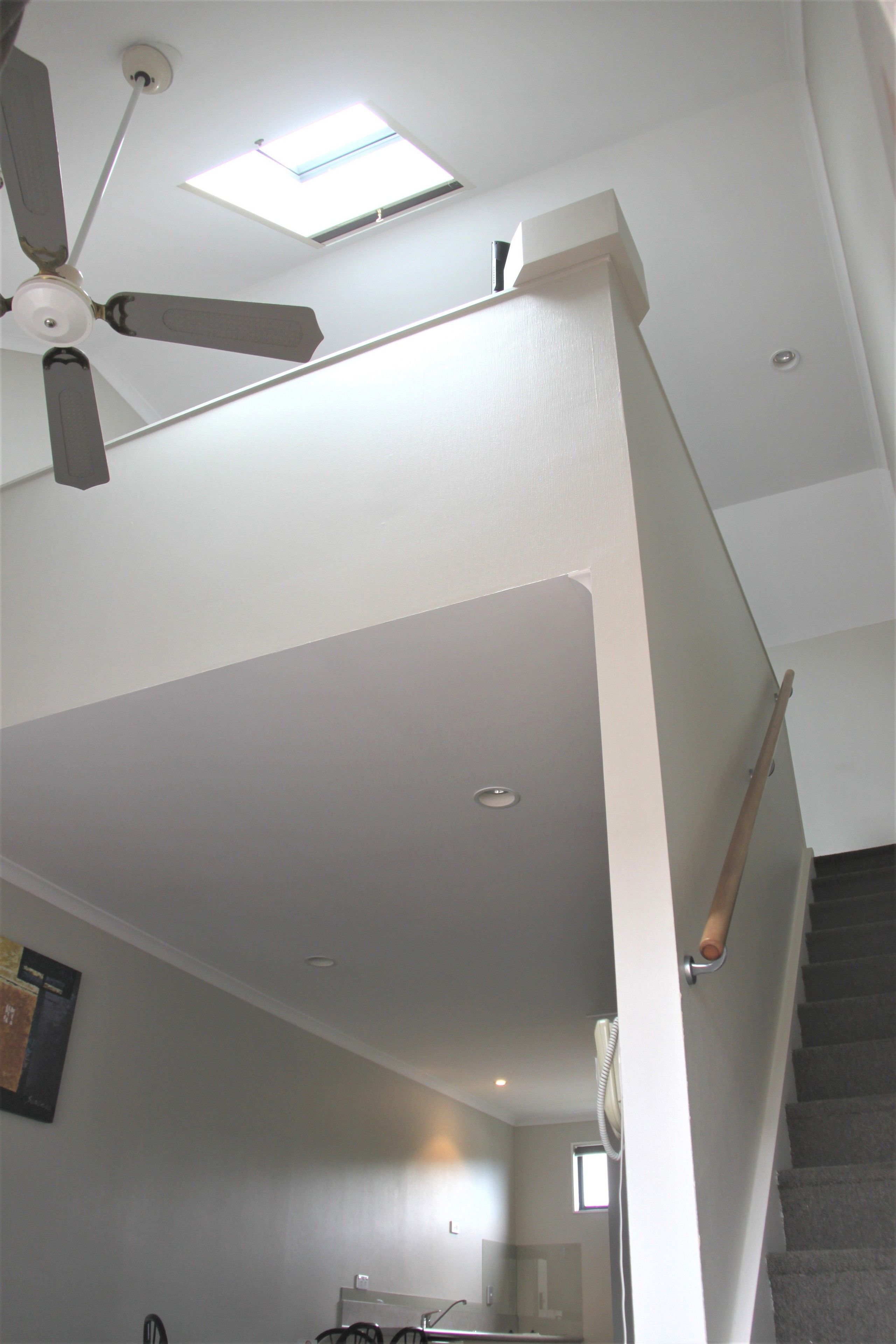 Una escalera con barandilla, ventilador de techo y tragaluz.