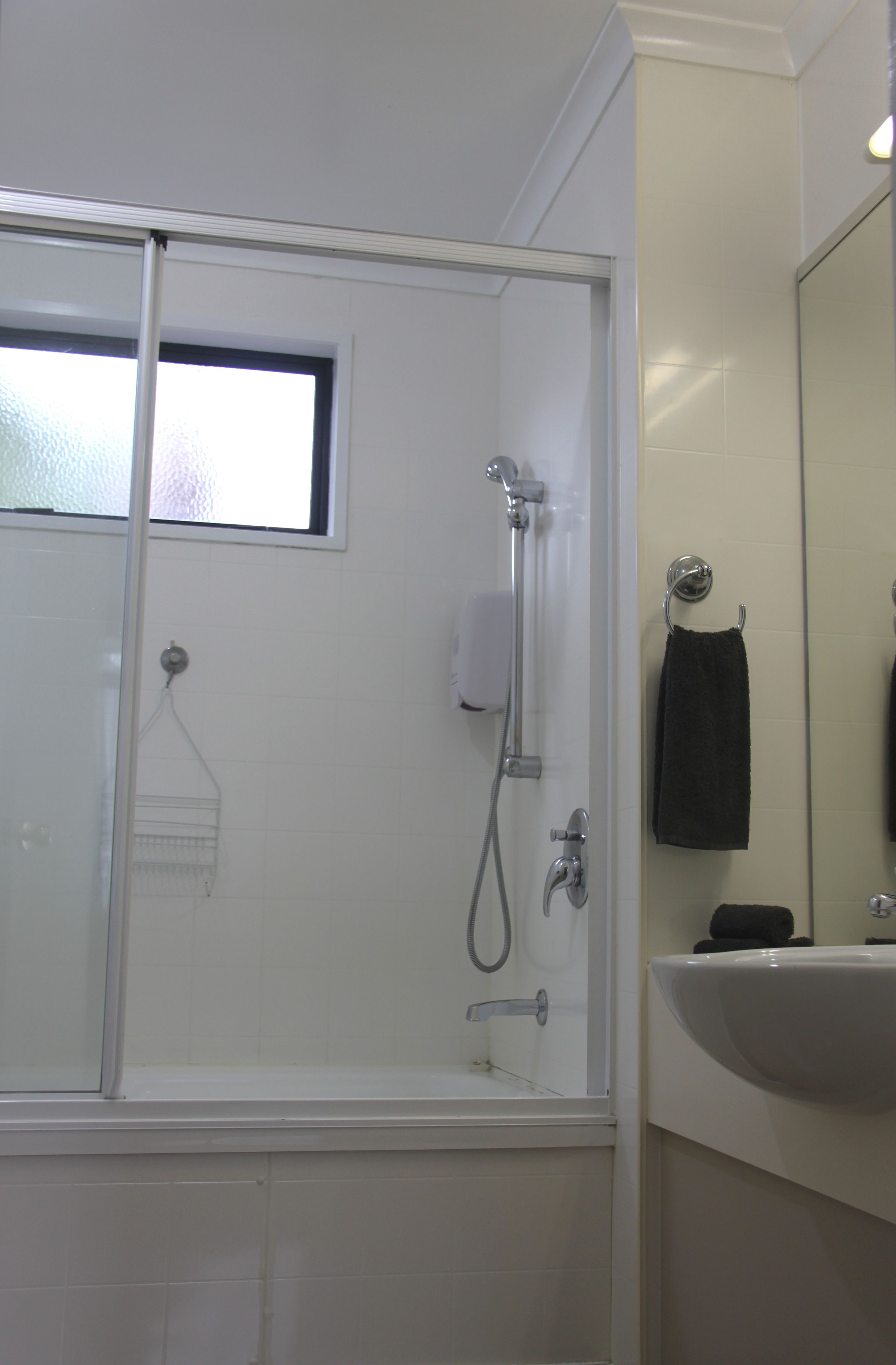 A bathroom with a glass shower enclosure, a sink, and a towel hanging on the wall.