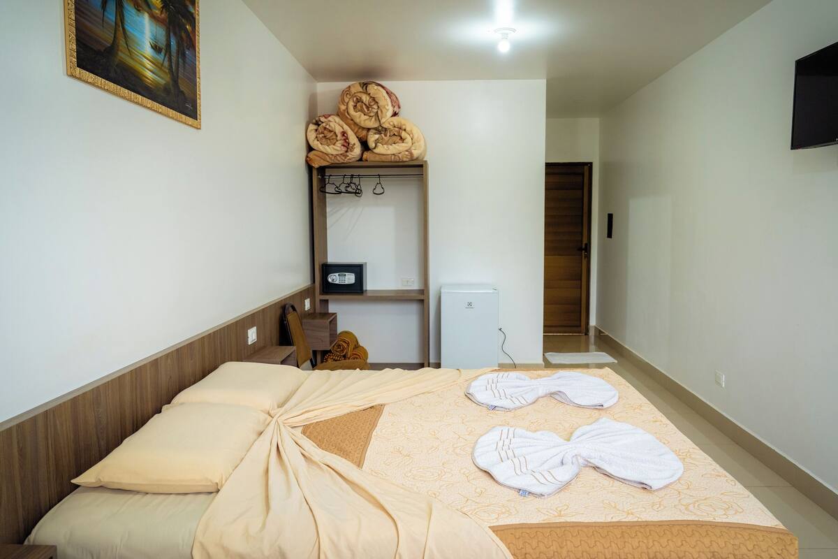 A hotel room with a bed, towels, a small refrigerator, and a TV on the wall.