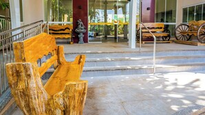Un banc en bois et une statue se trouvent devant un bâtiment dont un escalier mène à une porte en verre.