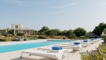 Una piscina al aire libre, sombrillas, sillones reclinables de piscina