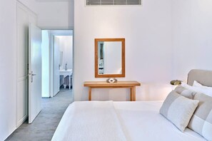 Habitación de hotel con una cama grande, una mesita de noche con espejo y vista al pasillo.