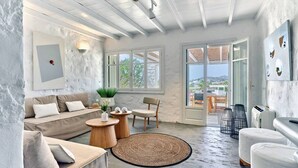 A modern living room with a sofa, armchairs, a coffee table, and a large window. - Stagones Luxury Villas (Paros)
