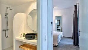 A modern bathroom with a shower, a sink with a mirror, and a bedside table with a plant. - Stagones Luxury Villas (Paros)