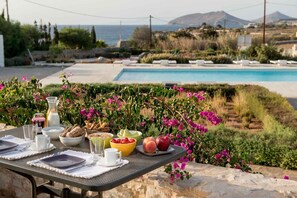 Una mesa de comedor dispuesta con alimentos para el desayuno y vistas a una piscina y un paisaje.