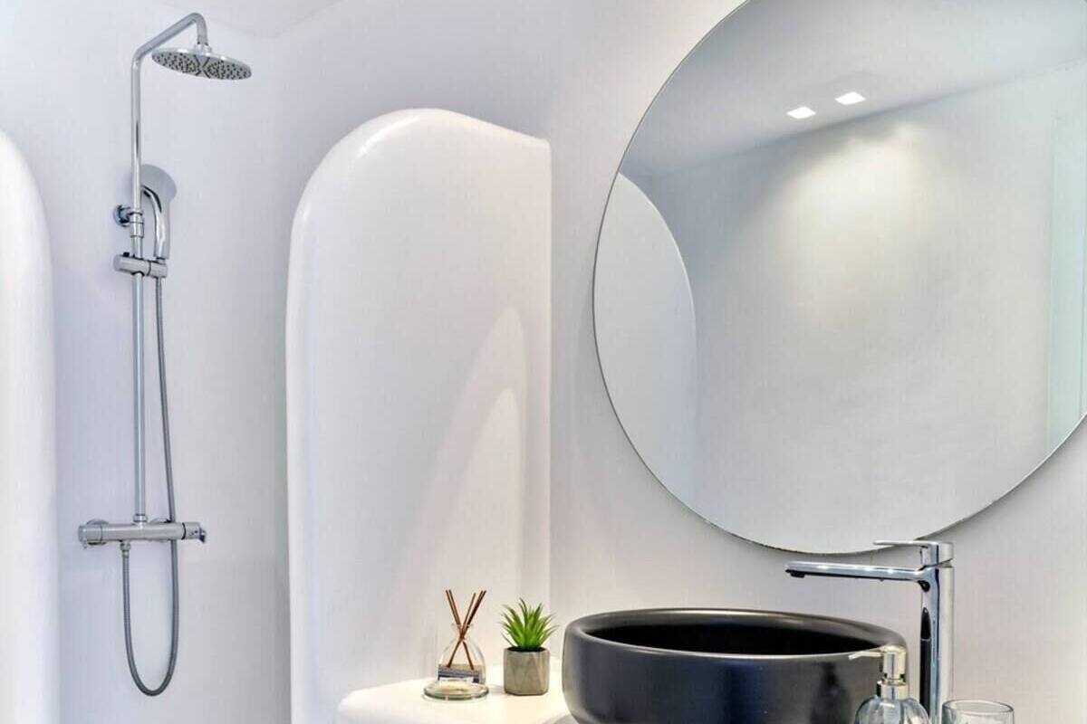 A modern bathroom with a bathtub, a shower, a round mirror, a black basin, a wooden shelf, and a small plant.