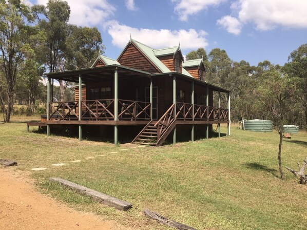 A wooden cabin with a porch and stairs, surrounded by grass and trees. - Manzanilla Ridge (Lovedale)