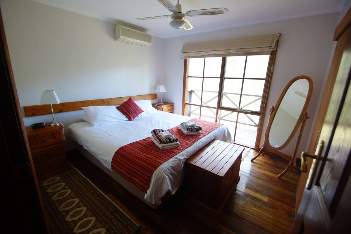 A hotel room with a bed, bedside table, lamp, window, and a ceiling fan.
