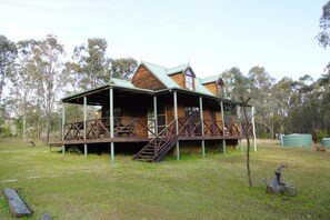 A wooden cabin with a covered porch and a staircase leading to the entrance. - Manzanilla Ridge (Lovedale)