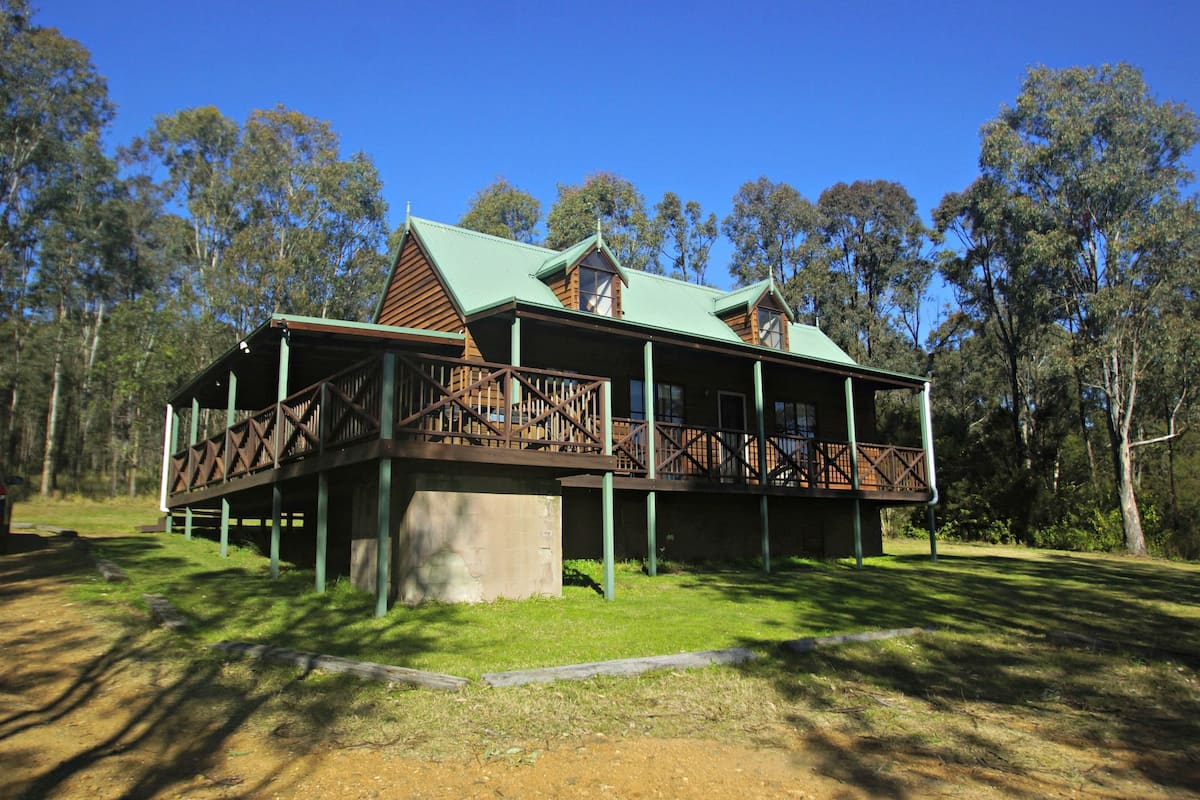 A two-story wooden building with a green roof, surrounded by trees.