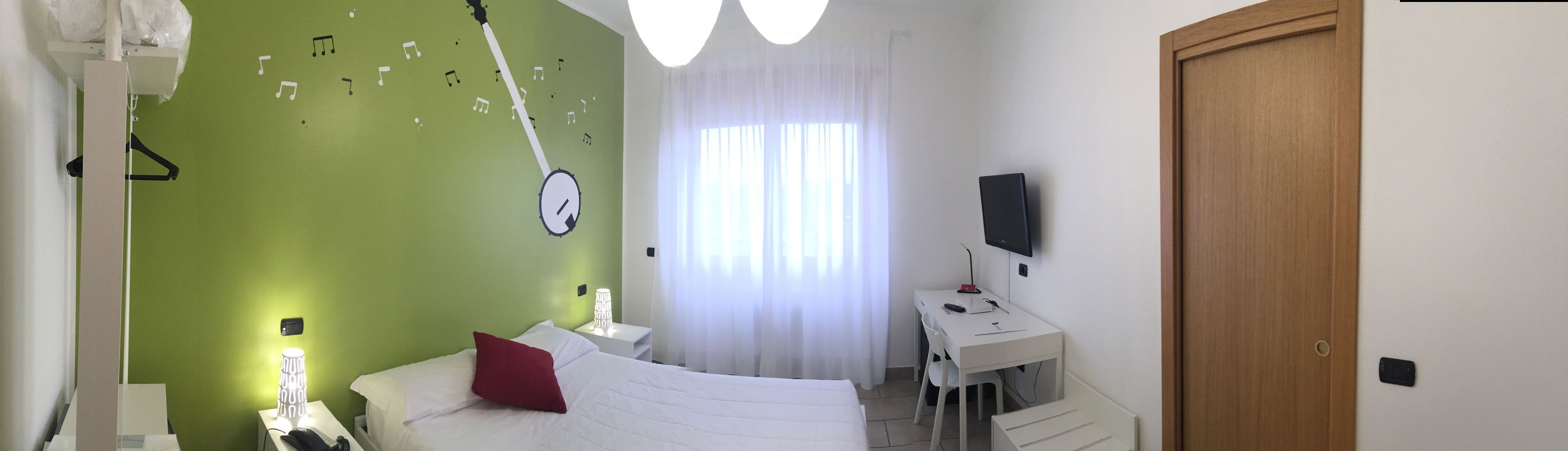 A bedroom with a bed, a desk, a TV, and a clock on the wall.
