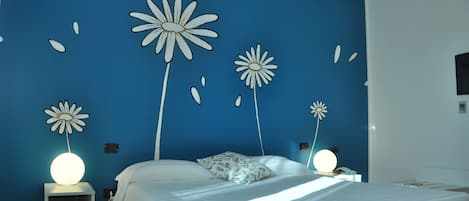 A bedroom with a blue wall, a bed with white bedding, and decorative flower wall art.