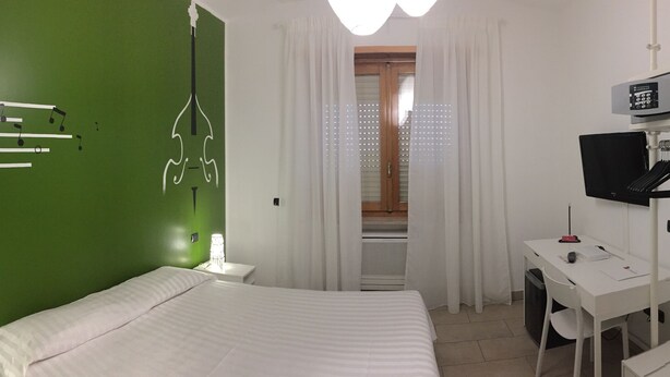 A bedroom with a green wall, a bed, a desk with a computer, a TV, and a mirror.
