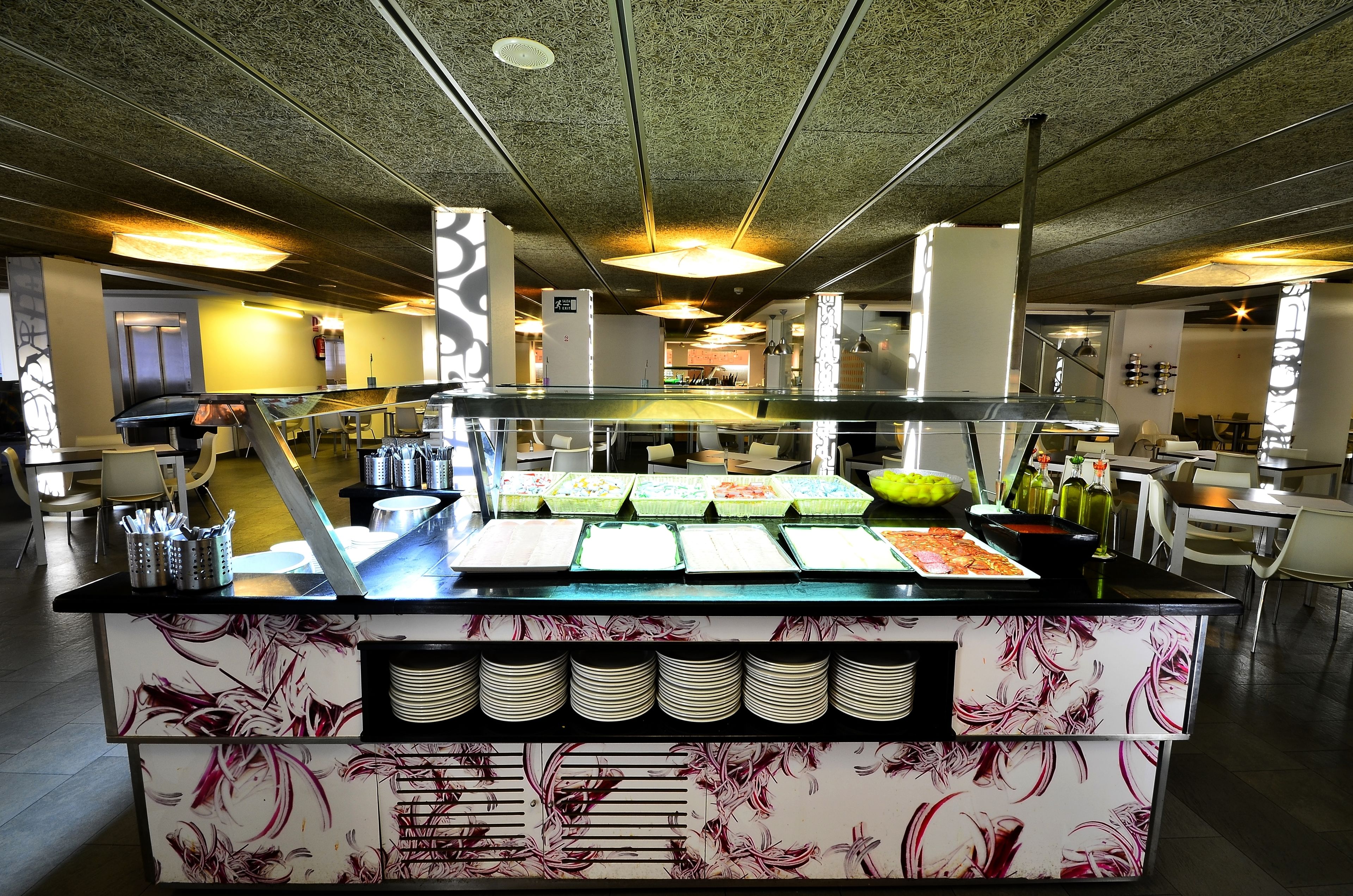 Ein reichhaltiges Buffet mit mehreren Speiseauslagen, einer Glasvitrine und einer Theke mit gestapelten Tellern.