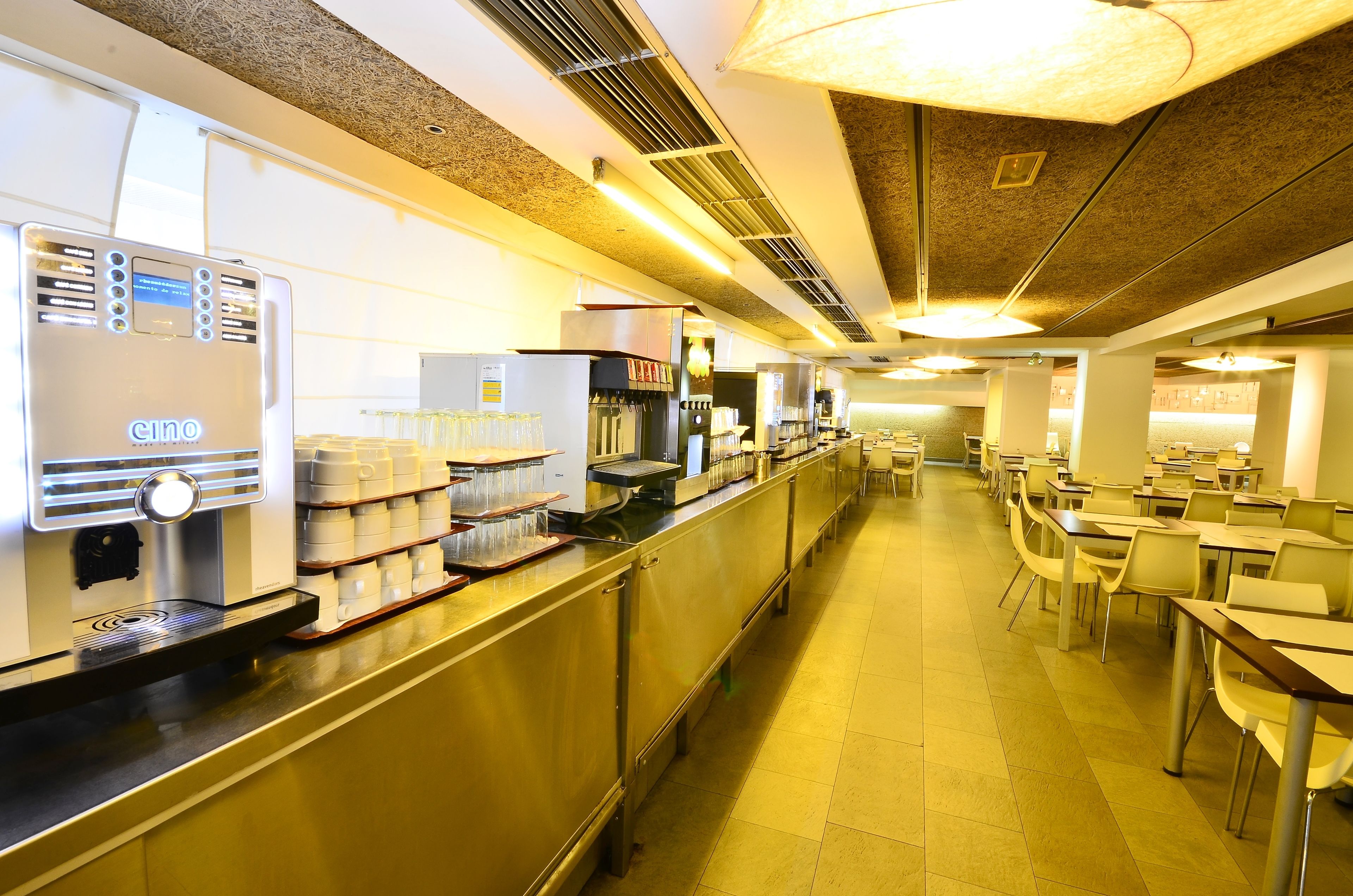 Una cocina industrial con electrodomésticos de acero inoxidable, incluyendo una máquina de café espresso Cino, y una encimera con cristalería.