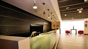 A reception area with a glass partition, a reception desk, and a seating area with two red chairs. - Hotel Sol & Sombra (Benidorm)