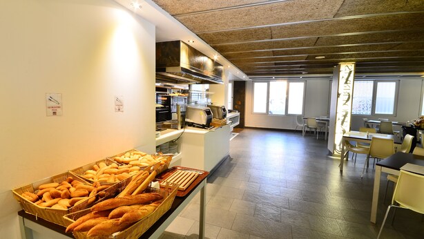 A buffet area with bread and pastries, a kitchen in the background, and a dining area with tables and chairs. - Hotel Sol & Sombra (Benidorm)