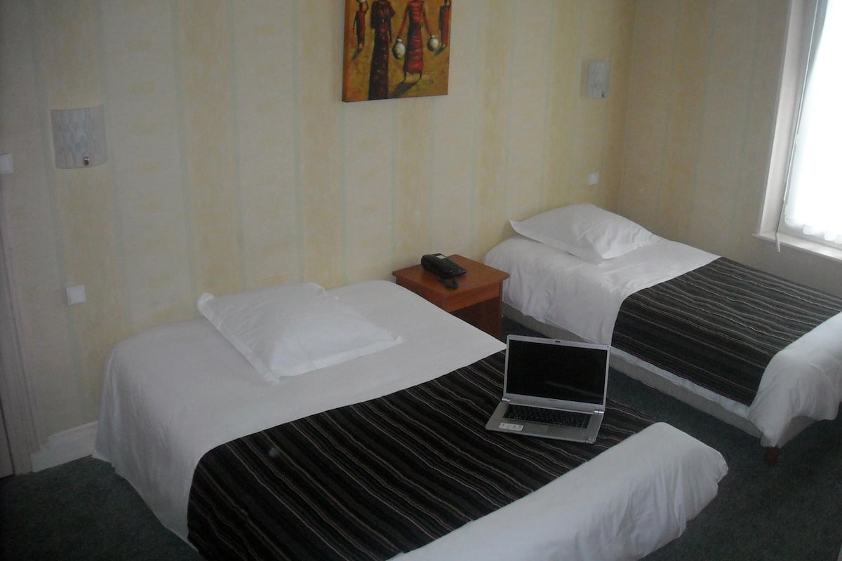 Habitación de hotel con dos camas, una laptop sobre una de ellas, un cuadro en la pared y una ventana con cortinas.