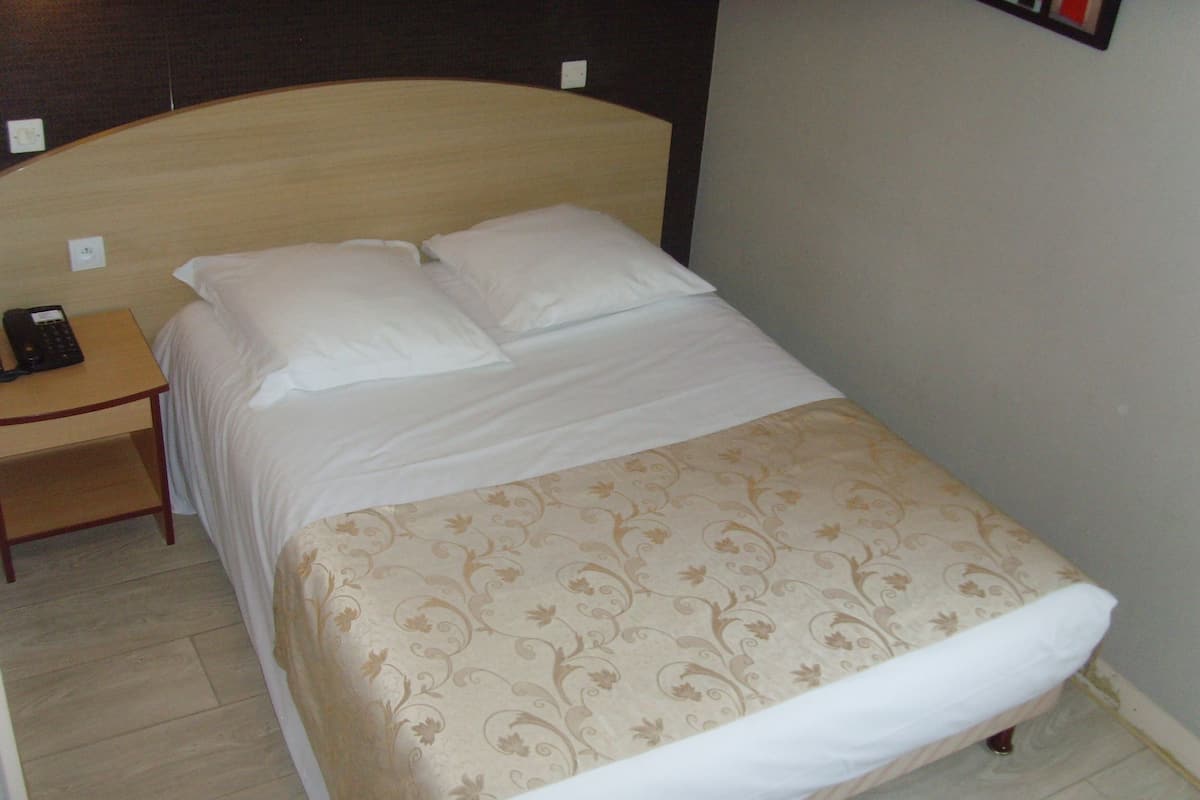 Una cama bien hecha con una colcha floral, una mesita de noche con teléfono y una lámpara de pared.