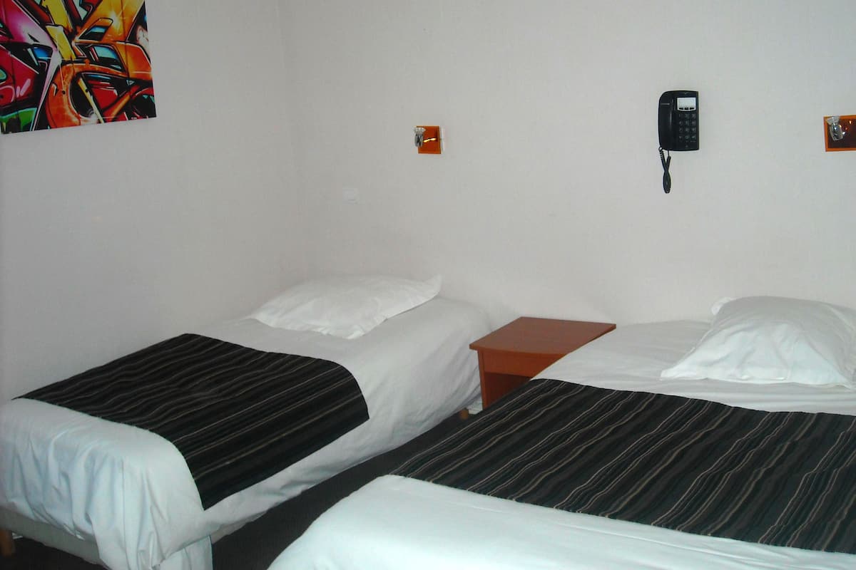 Habitación de hotel con dos camas, una mesita de noche, un teléfono y un cuadro abstracto de colores en la pared.