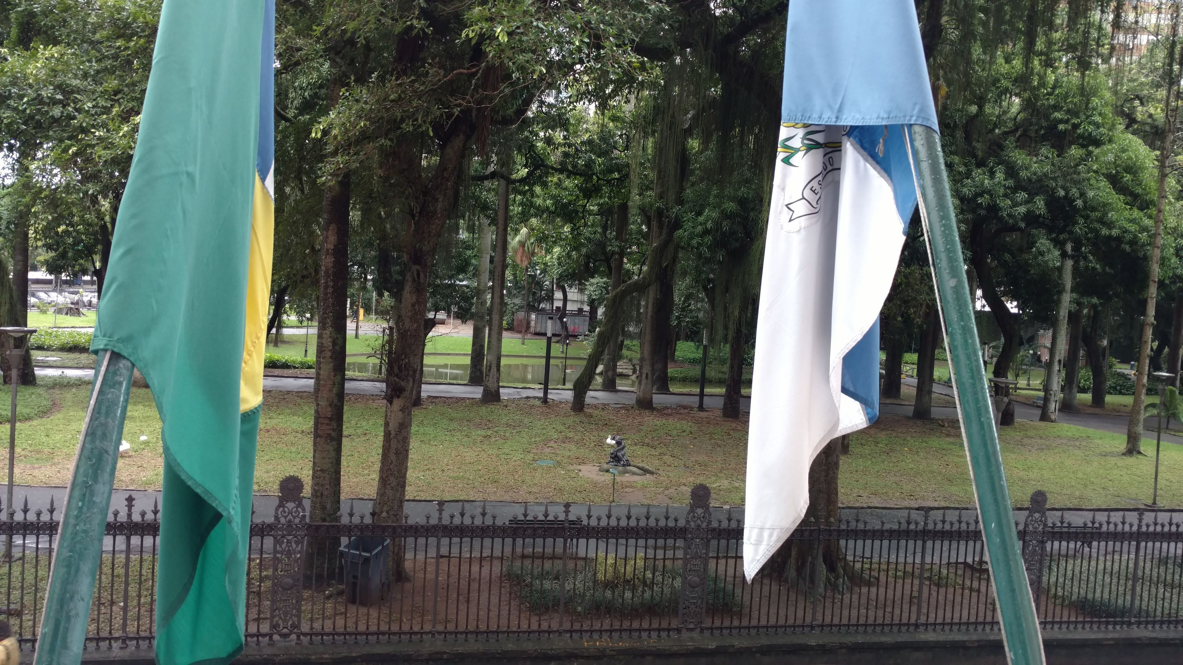 A park with a fountain, trees, and a fence.