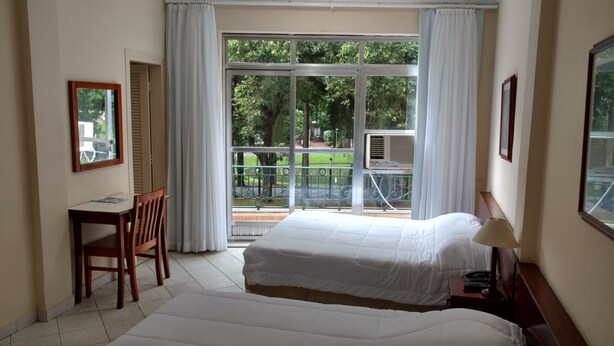 Quarto de hotel com duas camas, uma escrivaninha e uma cadeira.