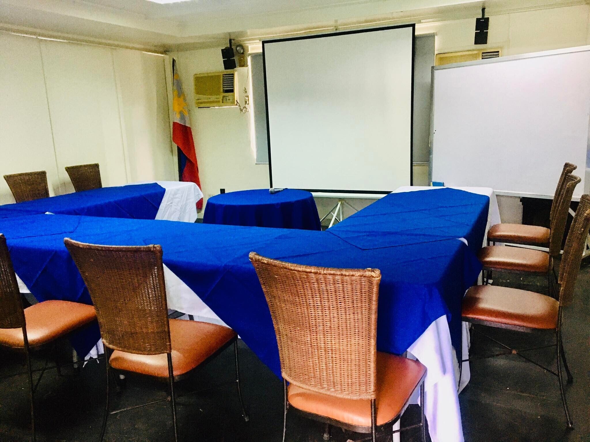 A conference room with a large table covered in blue cloth, surrounded by wicker chairs.