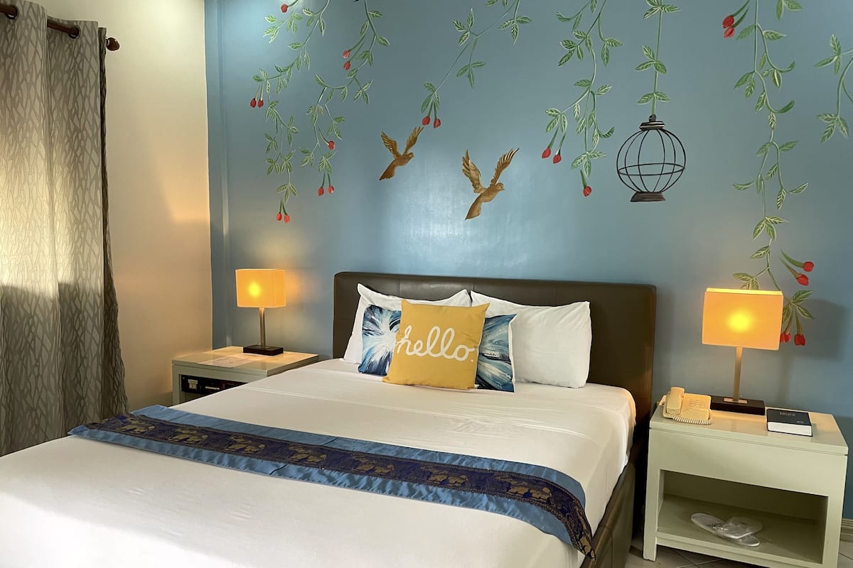 A neatly made bed with a blue and white bedspread, two bedside lamps, and a wall with a nature-themed mural.