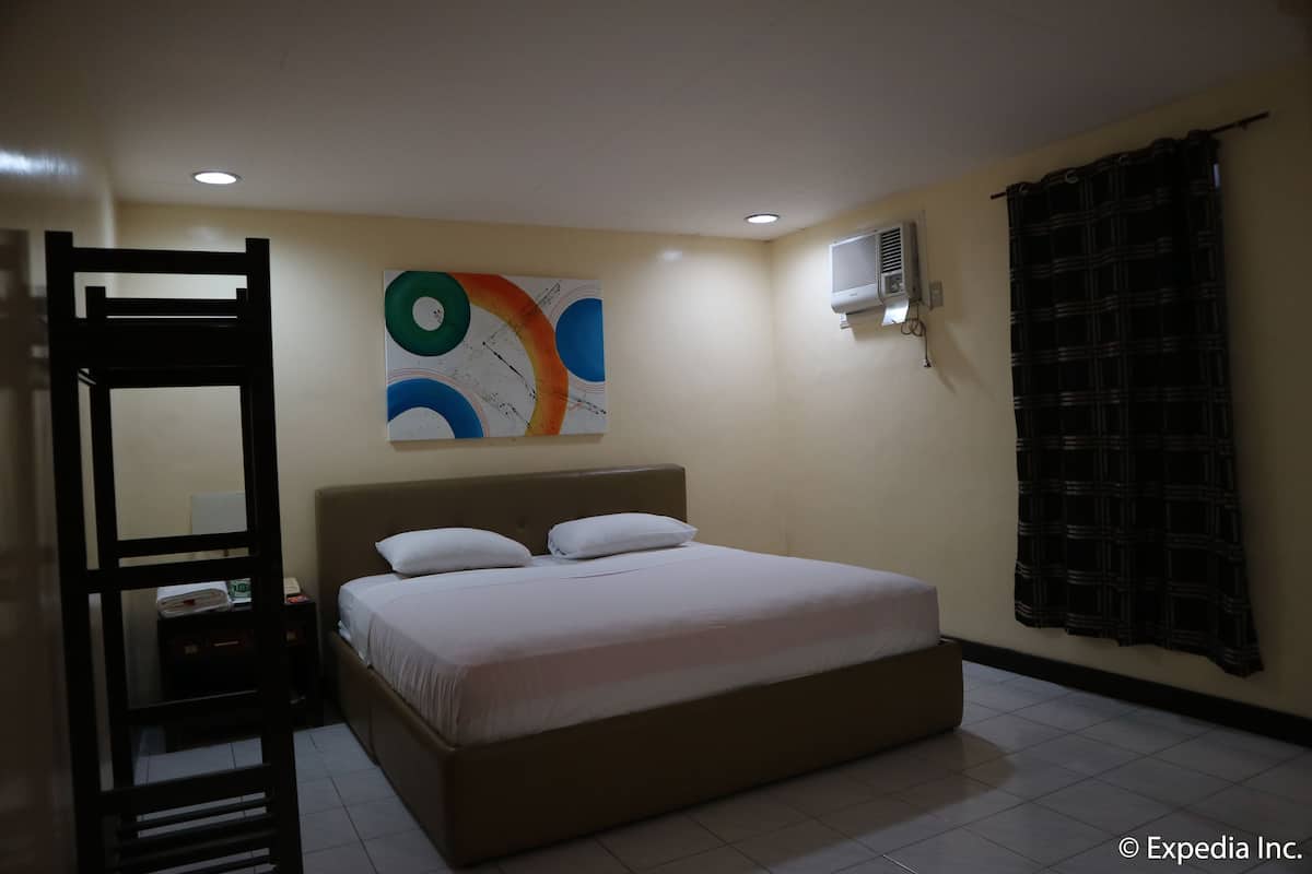 A bedroom with a bed, a wall-mounted air conditioner, a window with a curtain, and a painting on the wall.