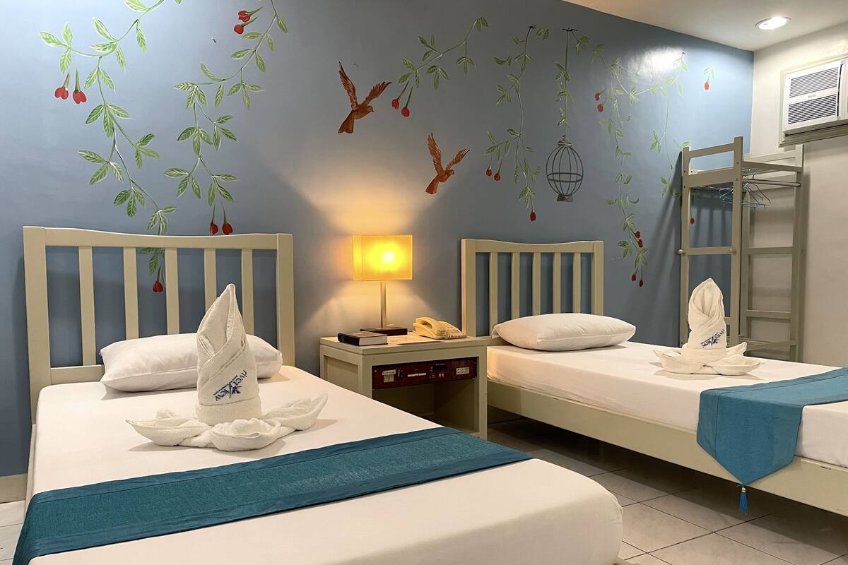 A hotel room with two beds, a nightstand with a lamp, a phone, and a ladder against the wall.