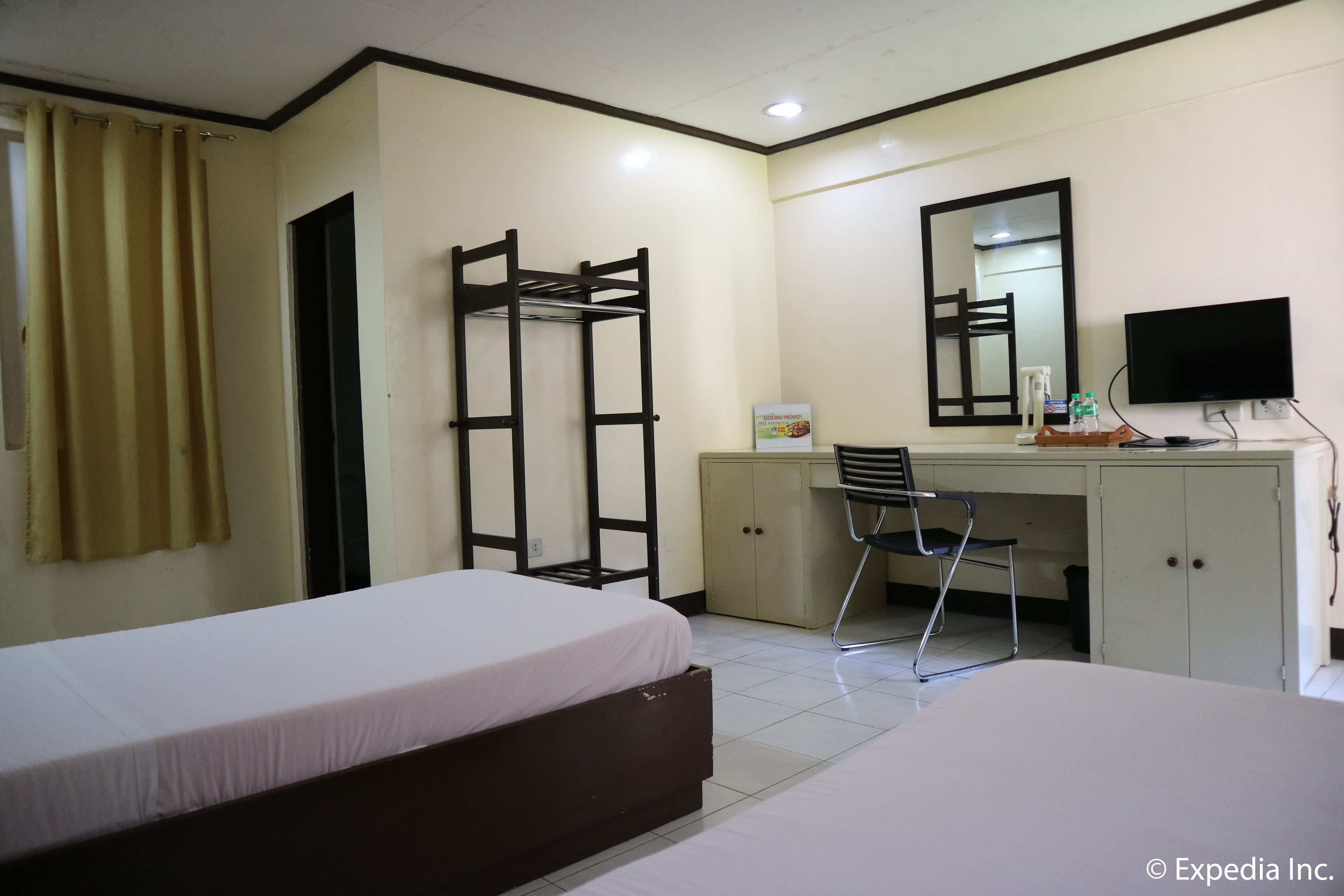 Habitación de hotel con dos camas, un escritorio, una silla, un armario, un espejo y un televisor.