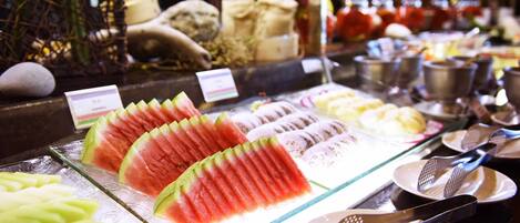 A display of various fruits and vegetables, including watermelon and green apples, arranged on a glass counter.