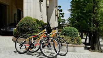 Deux vélos sont garés devant un bâtiment orné de colonnes, et une voiture est visible à l’arrière-plan.