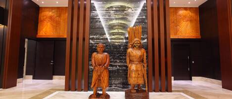 Un vestíbulo con dos estatuas de madera, una pared texturizada de color negro y paneles de madera.