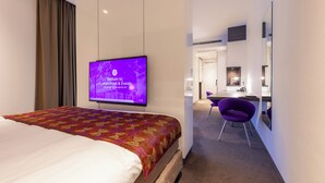A hotel room with a bed, a television displaying a welcome message, a desk with a chair, and a mirror.