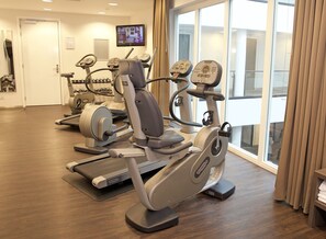 A gym with cardio machines, a TV screen, and large windows. - Lumen Hotel Zwolle (Zwolle)