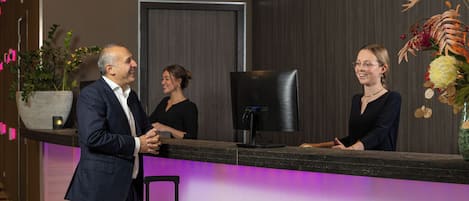 A reception desk with a modern design, a large monitor, and a potted plant.
