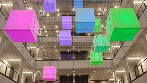 A modern interior with a high ceiling, geometric light fixtures, and a central staircase.