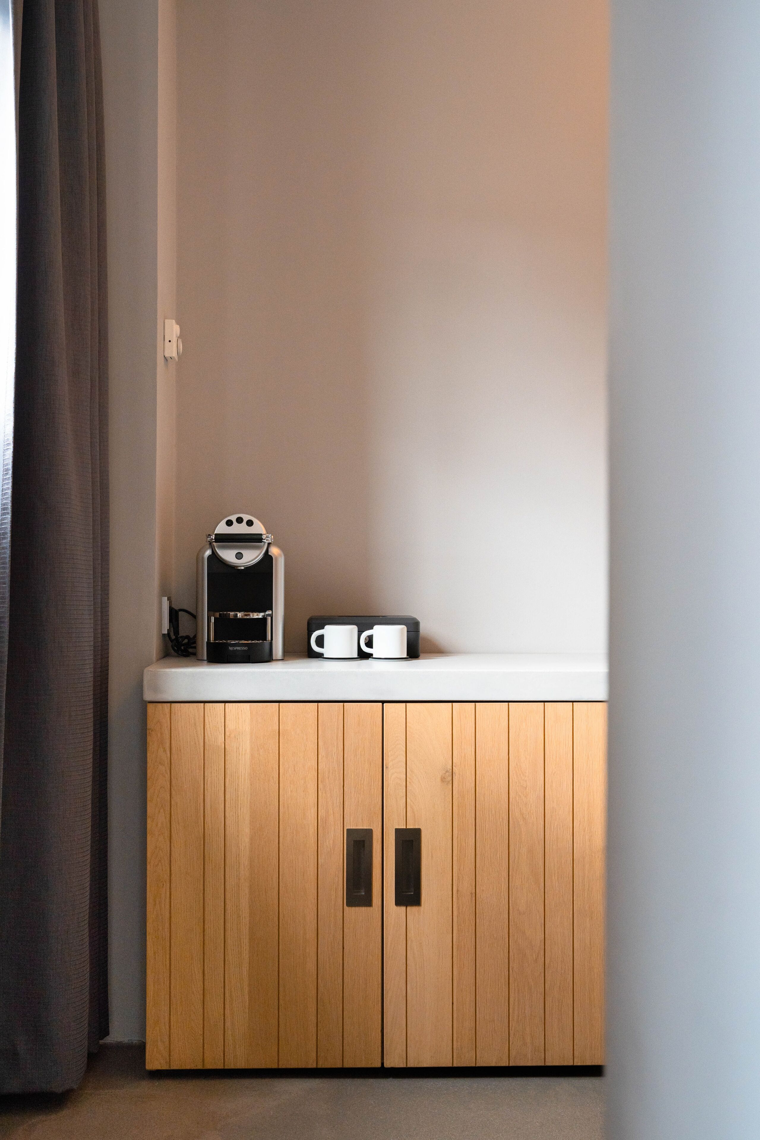 Une petite kitchenette équipée d’une machine à café, d’une tasse et d’une prise électrique sur un plan de travail blanc.