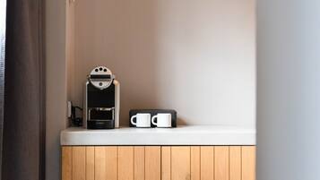 Une petite kitchenette équipée d’une machine à café, d’une tasse et d’une prise électrique sur un plan de travail blanc.