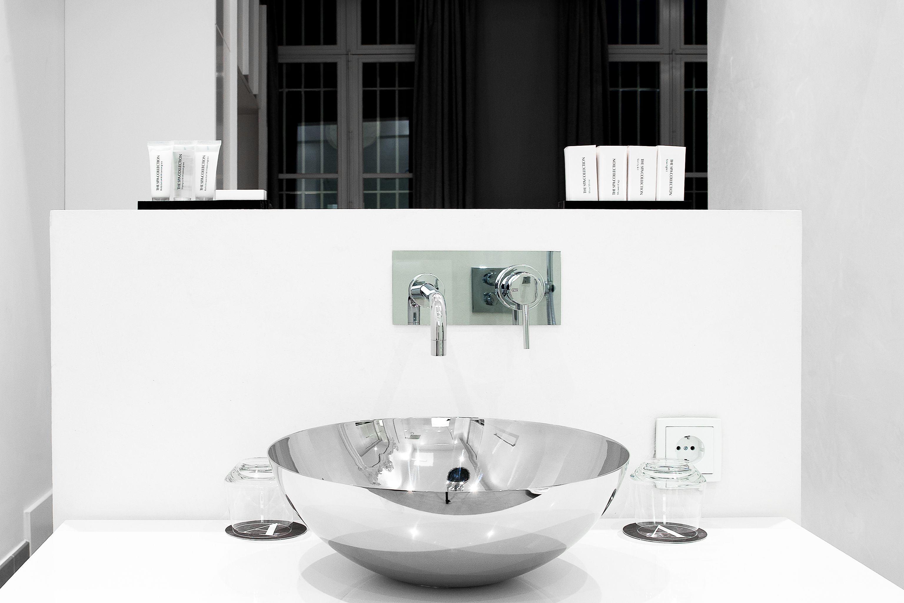 Een moderne badkamer met een grote, glanzende wasbak, een enkele kraan en een klein glazen potje op het aanrecht.